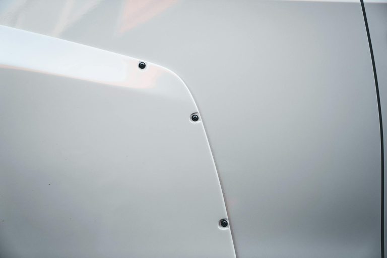 Detailed view of a white car's panel highlighting screws and smooth textures.